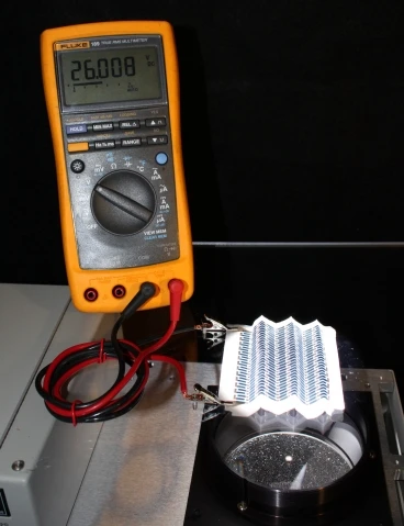 A paper solar cell that has been repeatedly folded is illuminated from below and connected to a voltmeter to demonstrate its output (26 V)(Image courtesy of the Gleason Lab)