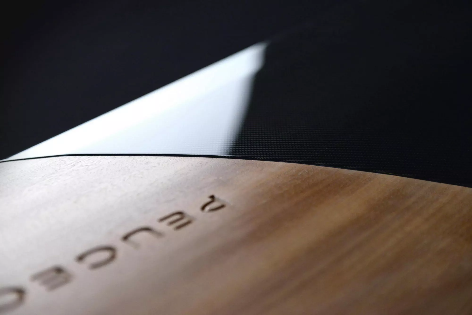 A sharp diagonal boundary line visually separates the wooden nose from the carbon fiber main body