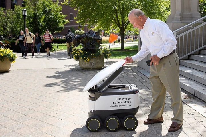 Purdue University president Mitch Daniels receives a robotic food delivery