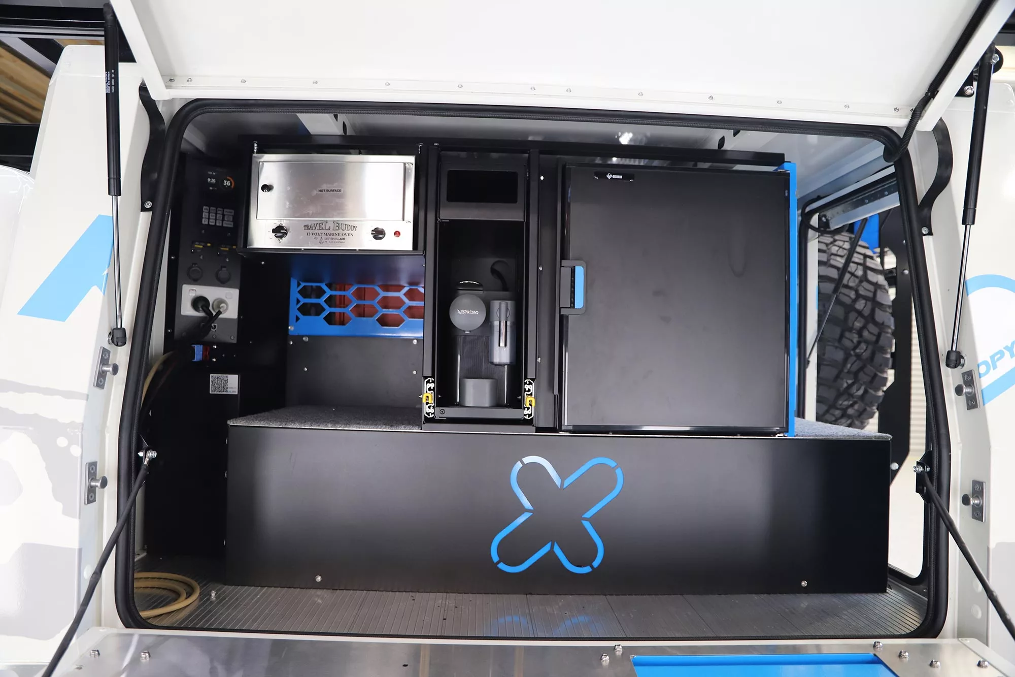 The passenger side of the canopy is dedicated to an available kitchen area with fridge/freezer on the right, coffeemaker in the center, electric oven top left/center, and electrical hardware on the left