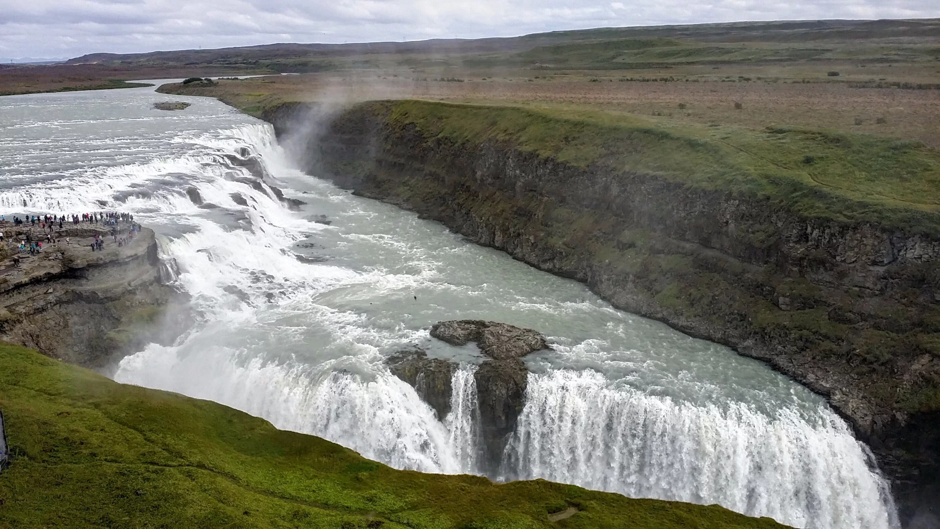 The multi-level Gullfoss waterfall was created when a flash flood raged through this area of southern Iceland during the last ice age. The force of water carved away soft sedimentary rock while leaving hard layers of basalt lava called dolerite on either side of the flow. The water that feeds Gullfoss today comes from the Lángjökull glacier about 40 km (25 mi) away. Because glacial water has a fair amount of sediment in it, it lends water a brownish tint, and in fact, Gullfoss is often called the "Golden Falls" due to this coloration.