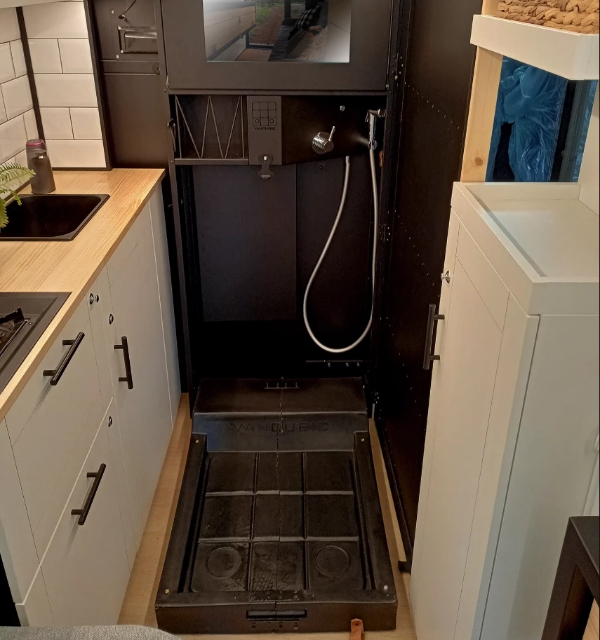 The shower cabinet hides behind the wood-slat door until it's needed, then the floor pan drops out for showering