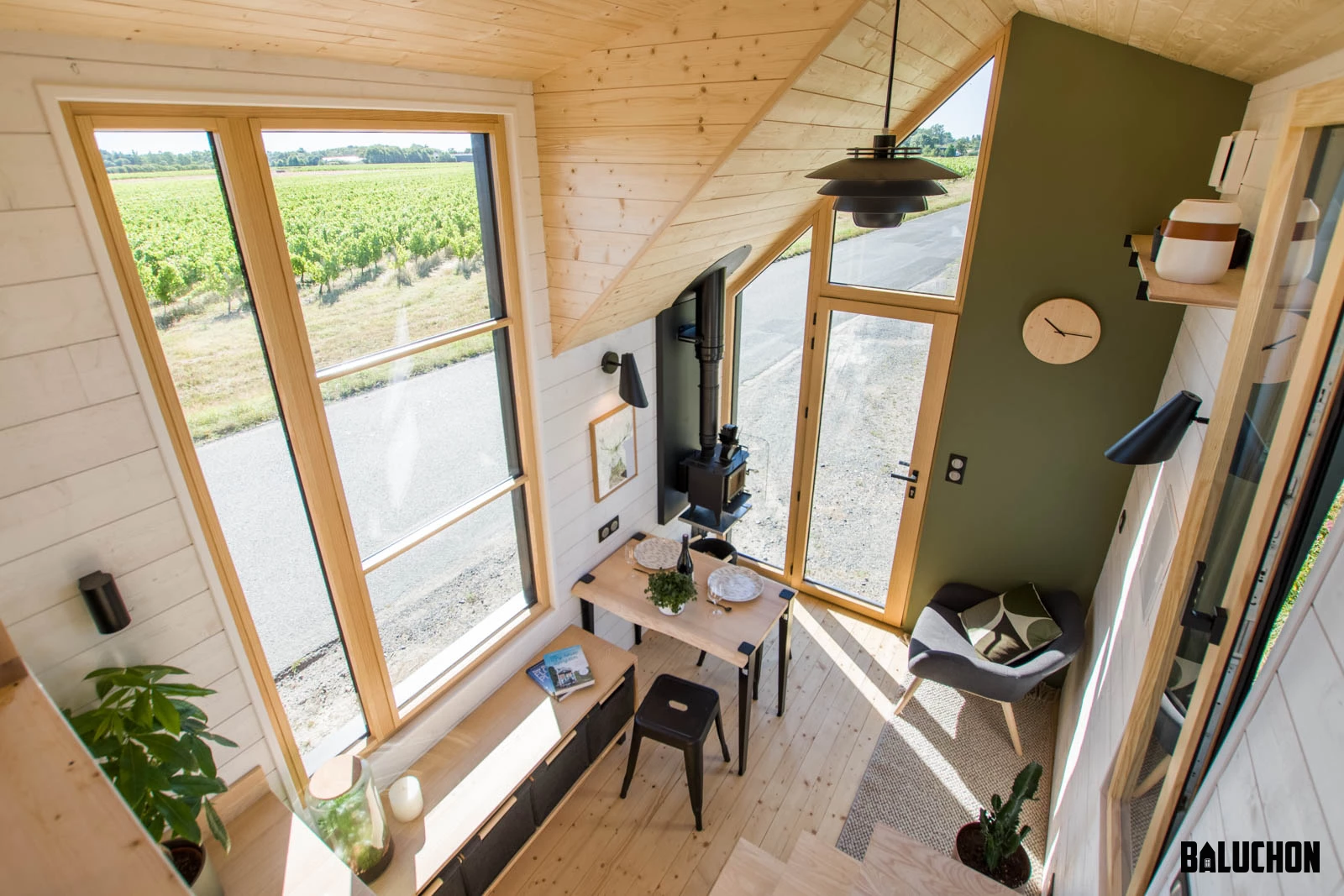 The Tiny House Sauvage's living room includes some seating, a dining table, and a very small wood-burning stove