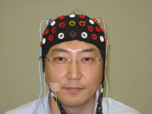 The EEG cap contains a array of electrodes to allow taping into different areas of the brain over the skull. The driver is also wearing a cheek puff detector to allow reliable stopping of the wheelchair (Photo: RIKEN)