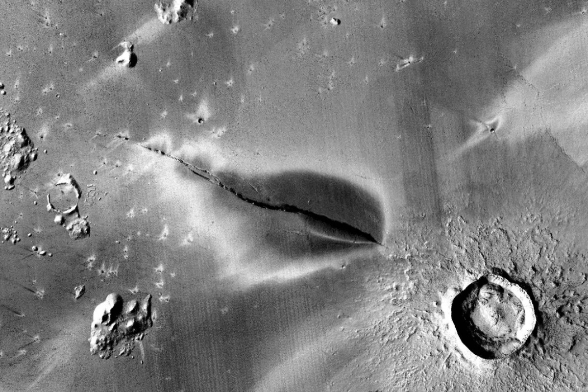 The dark area appears to be a relatively recent volcanic deposit, and the large crater nearby may be connected