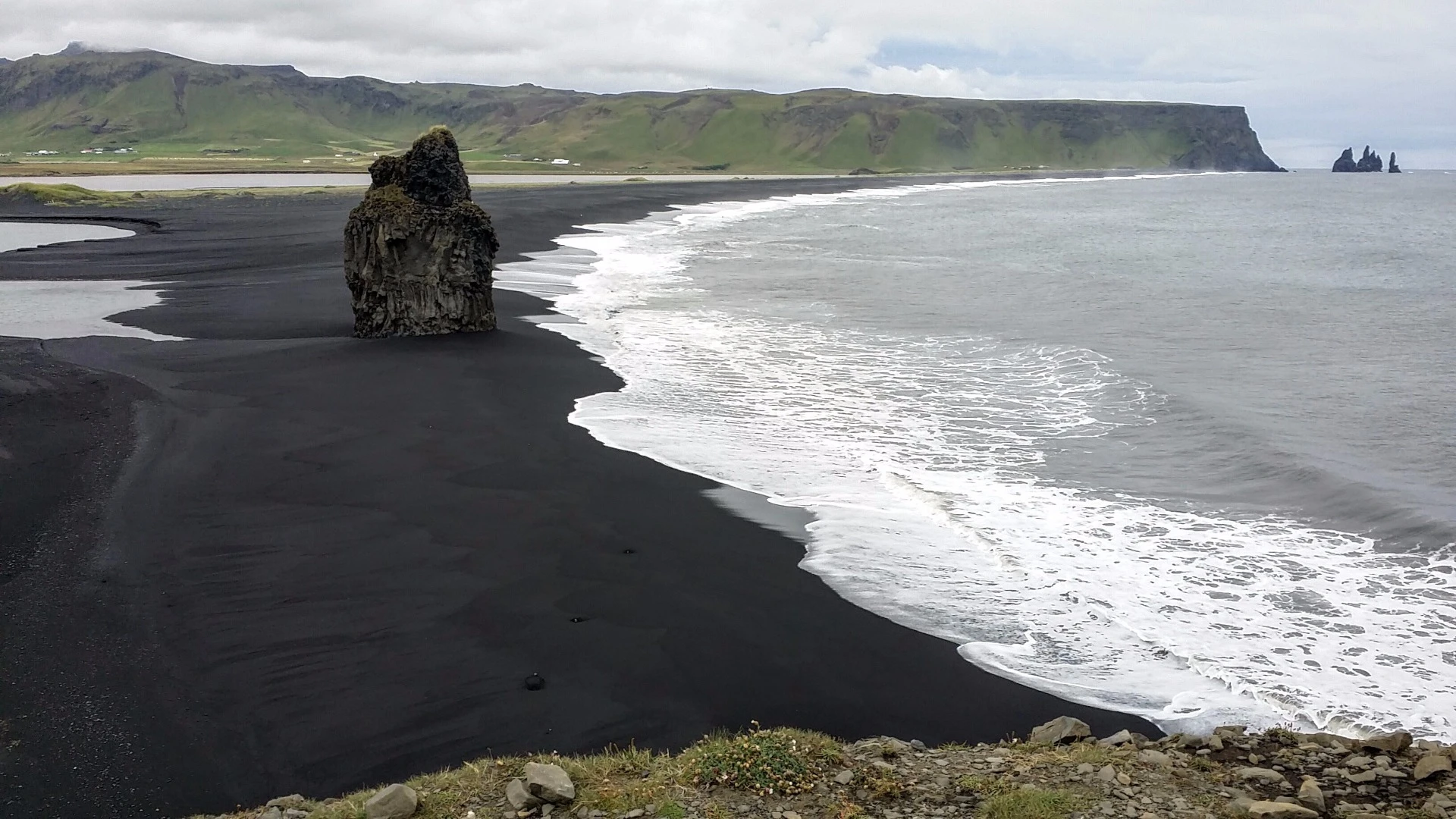 This picture was taken from the 120-m-high (394 ft) Dyrhólaey peninsula in the south of the country. The peninsula was formed partly from an undersea eruption approximately 80,000 years ago. The tall formation on the beach, as well as the distant sea stacks in the upper right, known as Reynisdrangar, were formed as softer stone was eroded around harder basaltic compositions. The legend of Reynisdrangar says that two trolls were pulling a three-masted ship to shore when the sun rose and turned them to stone.