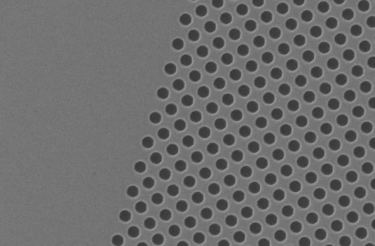 This scanning electron microscopy image details a portion of the photonic crystal structure used for wavelength demutiplexing. A periodic array of holes with a 220 nanometer radius is etched through the top silicon layer of a silicon-on-insulator wafer.