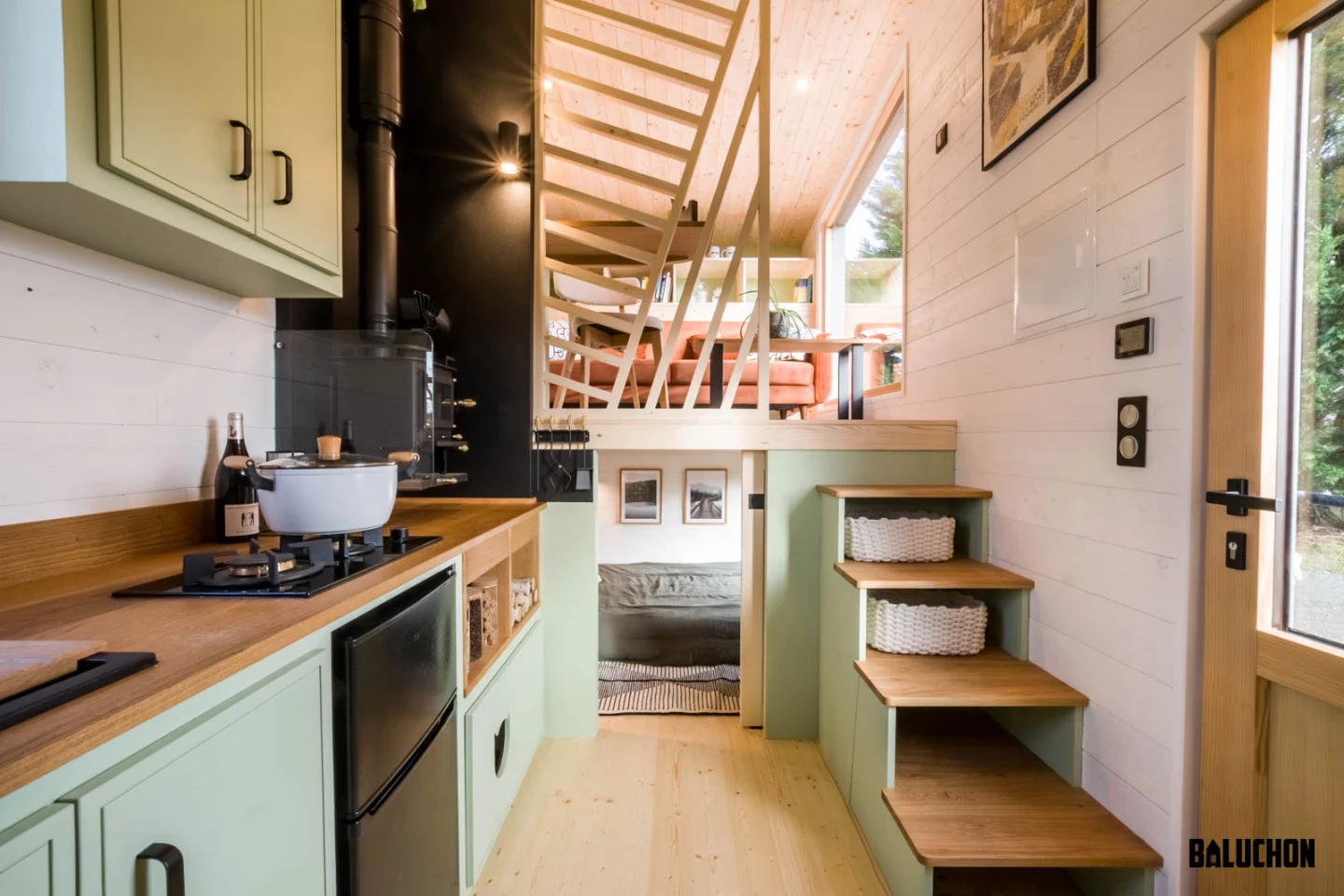 The Ellèbore tiny house's kitchen includes a mini fridge/freezer, two-burner propane-powered stove, sink, and a small wood-burning stove for warmth