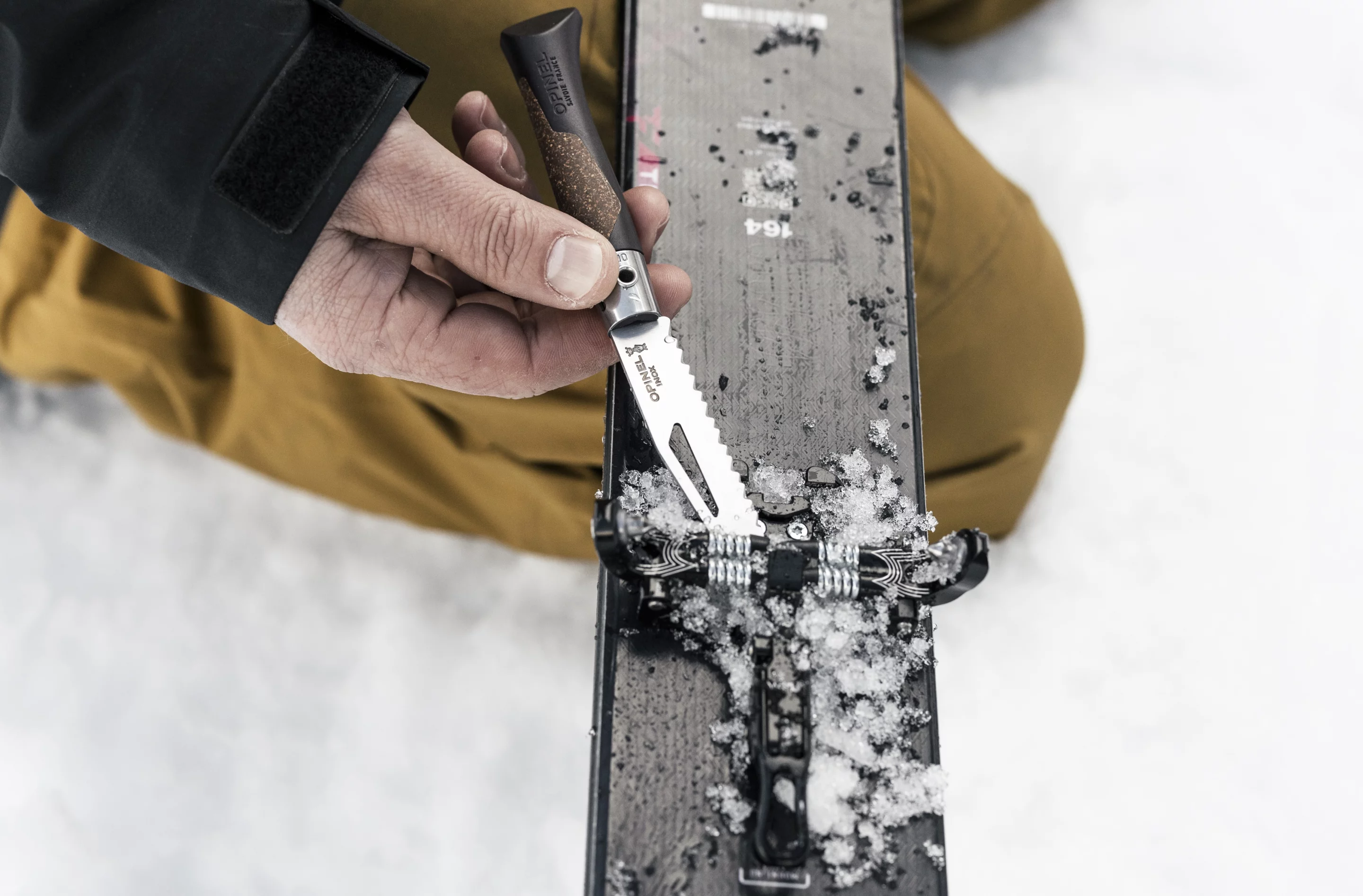 Using the scraper tip to remove snow and ice from a ski binding