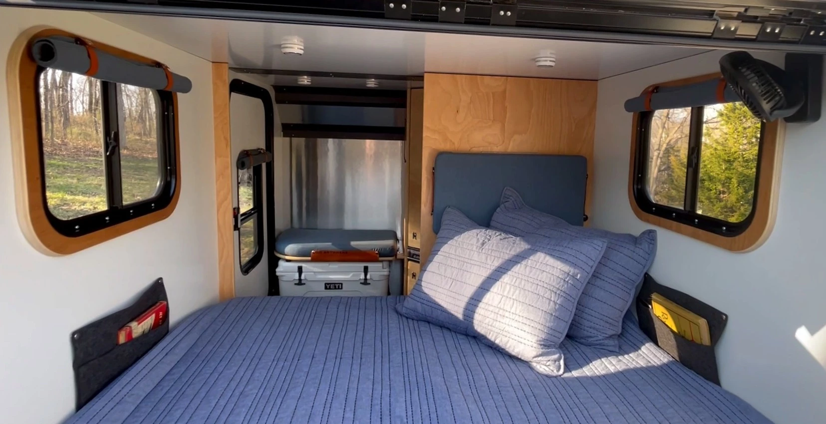The Campinawe interior includes a queen-size bed, storage cabinet and a bench seat over top the Yeti cooler