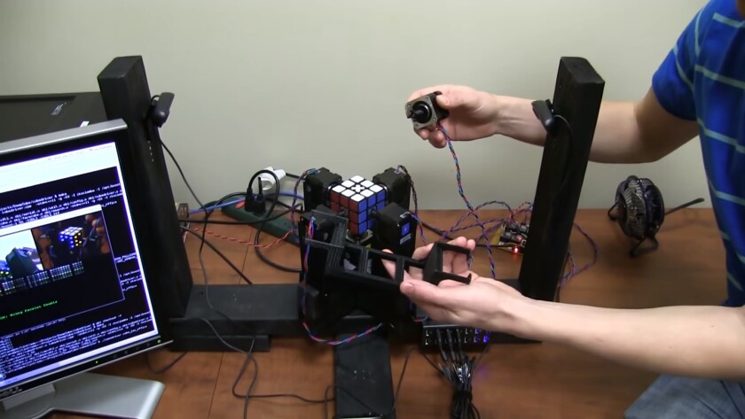 The stepper motors rest in a 3D-printed frame and have 3D-printed feet on the end, which slot into sinkholes drilled around the center squares on each side of a Rubik's Cube