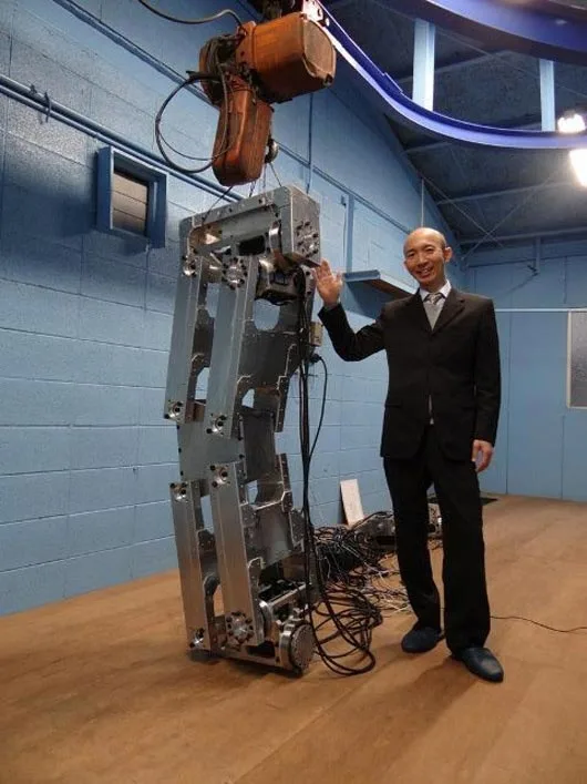 Hajime Sakamoto stands next to one of the legs of his 4 meter tall robot during construction