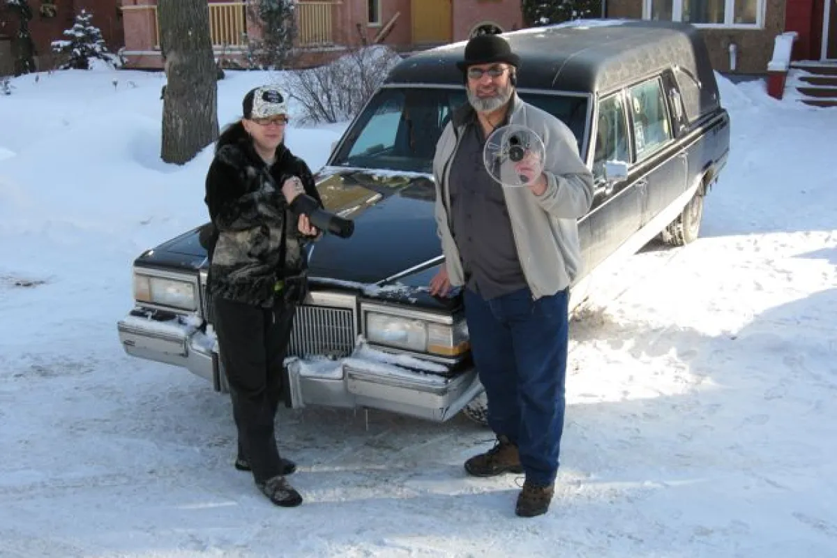 Paranormal investigators Rona Anderson and Ben Myckan sporting some of their ghost-hunting gear in front of their hearse, Nocturna