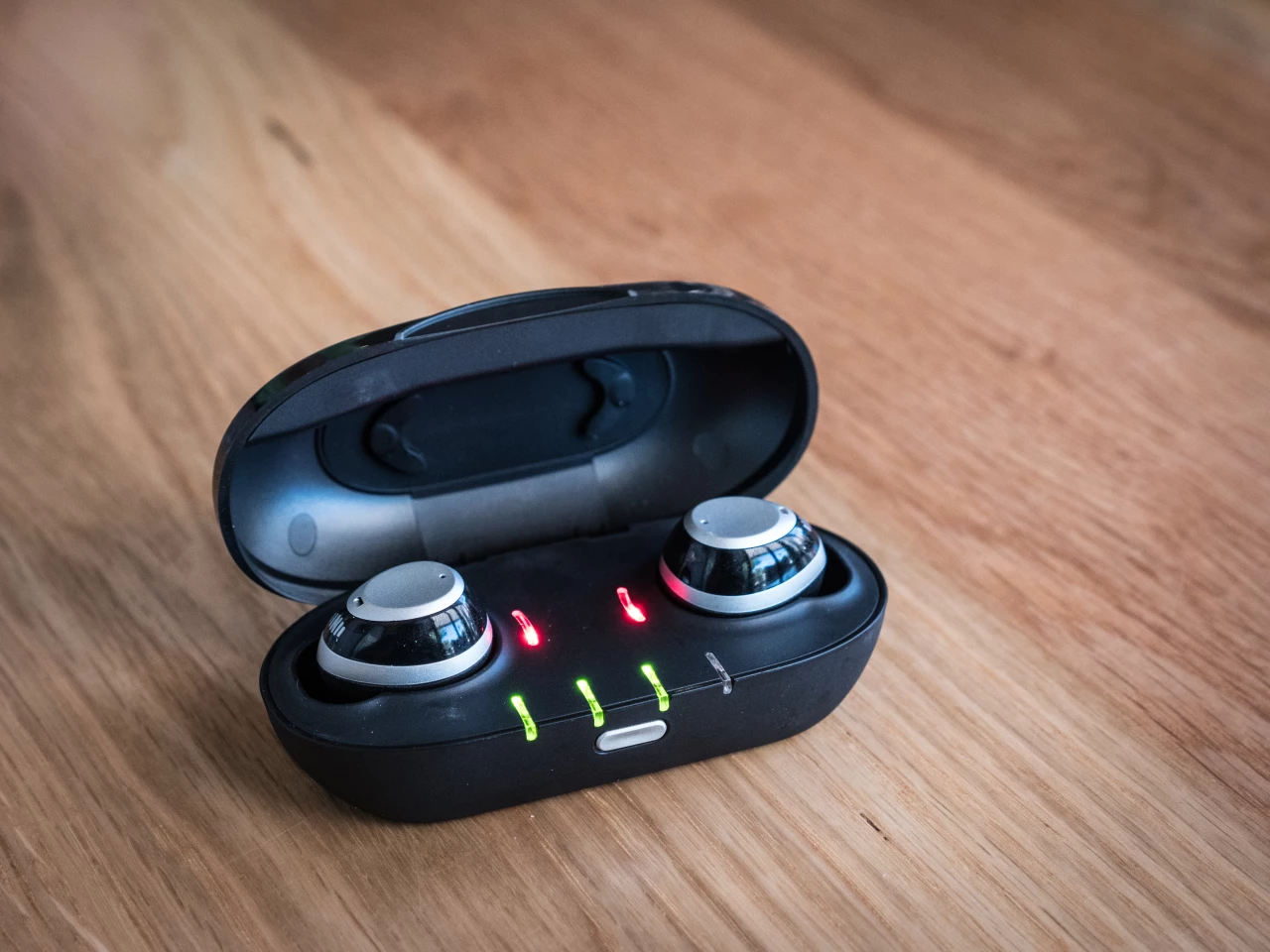 Nuheara IQbuds in their charging case. Red lights denote that the buds themselves are charging. Green lights indicate that the case itself has 3/4 charge remaining