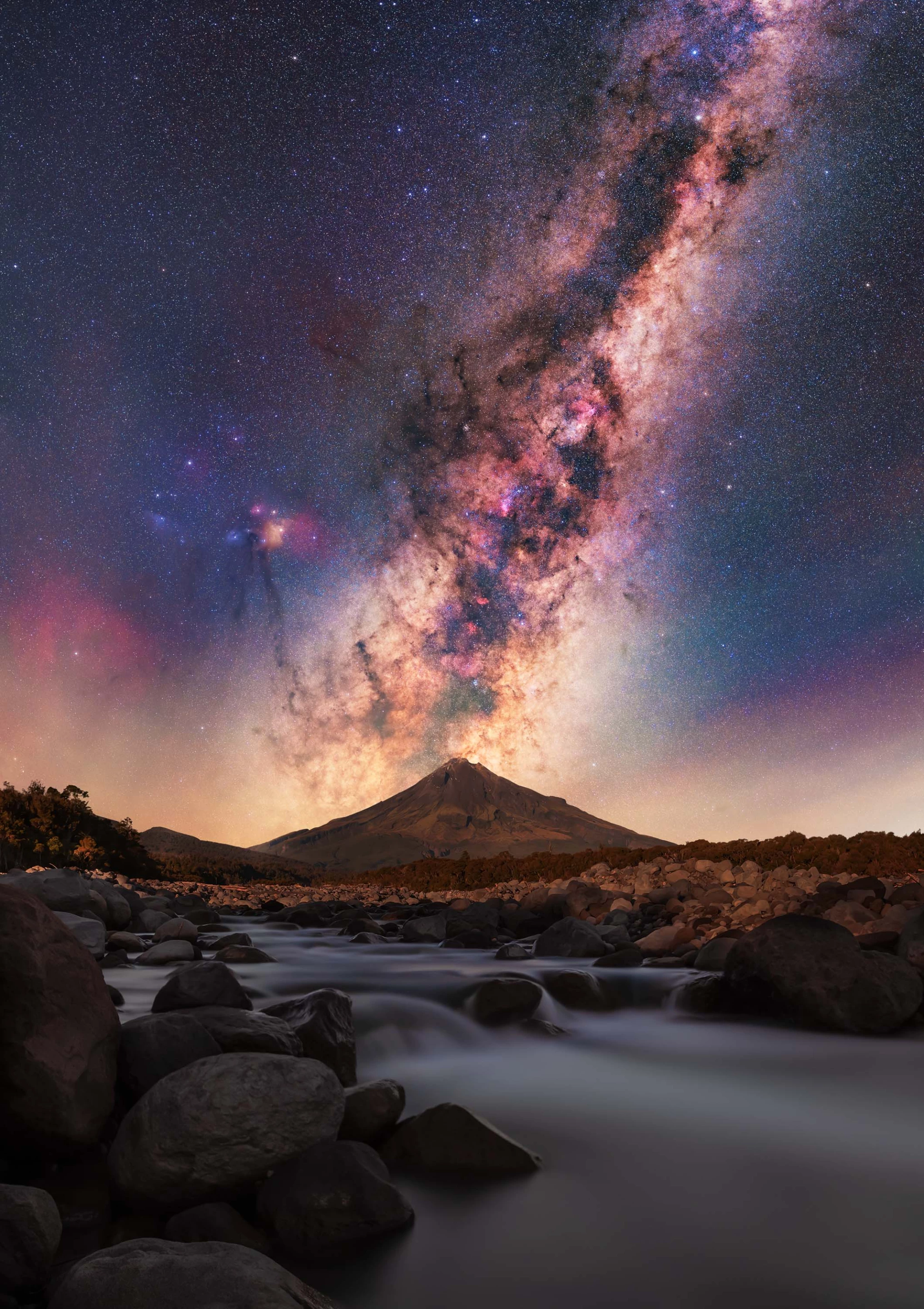Milky Way Rising over Stony River & Mt Taranaki by Brendan Larsen, taken in New Zealand. The photographer waited until 2:30 in the morning for the Milky Way to line up with Mount Taranaki, capturing some astonishing colors in the process