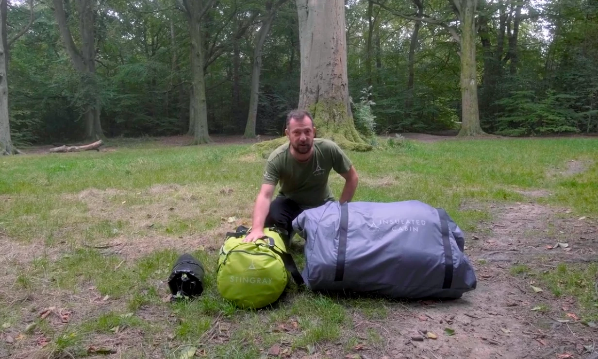 The yellow package on which the presenter's hand rests is the actual Stingray tree tent, while the huge gray one to the viewer's right is the Insulated Cabin
