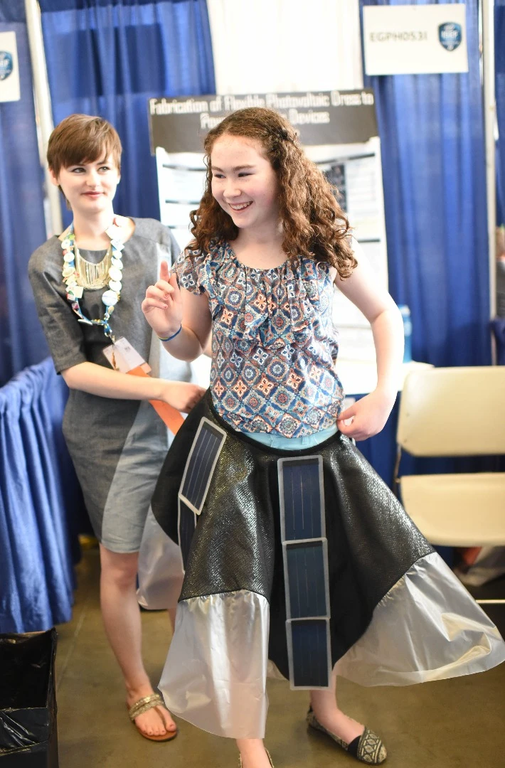 Ohio teenager Allison Clausius (left) holds her cellphone-charging dress at the waist of a young girl during the 2015 Intel International Science and Engineering Fair