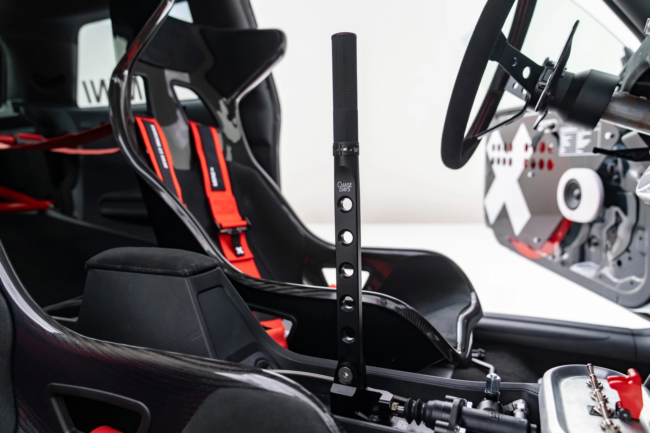 The Machina features stripped-back door panels with prominent white 'X' patterns next to a waxed fabric dashboard with a lived-in patina, and an exposed roll cage featuring 5-point racing harnesses