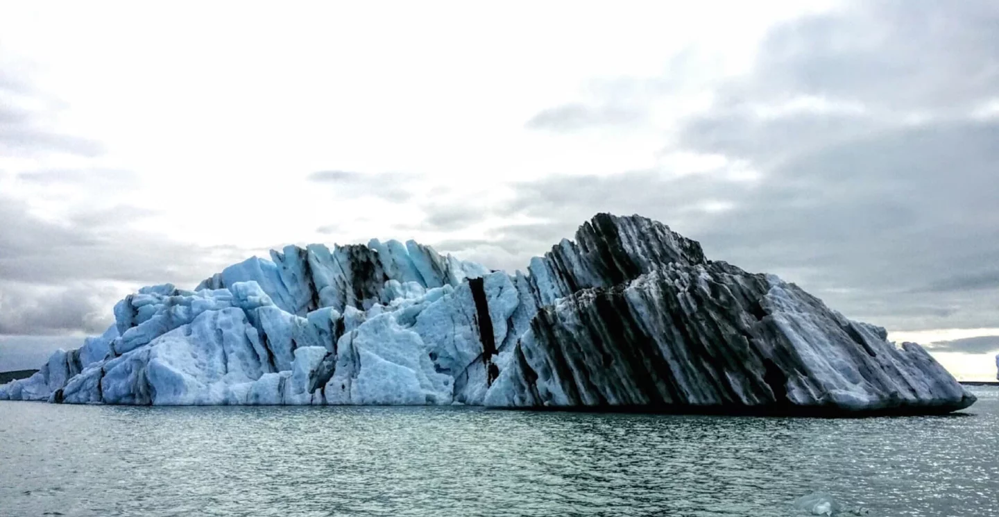 The color of an iceberg can tell you a lot. In this berg, the stripes of black represent volcanic eruptions that spewed ash on top of ice over time. The blueish tint to the ice shows that the iceberg flipped over recently. That's because when the ice first calves from the glacier, it is compacted so tightly that light coming through it takes on a blue hue. After the iceberg flips over, as they do from getting top heavy, the ice eventually turns white as the sun creates tiny cracks in its structure.
