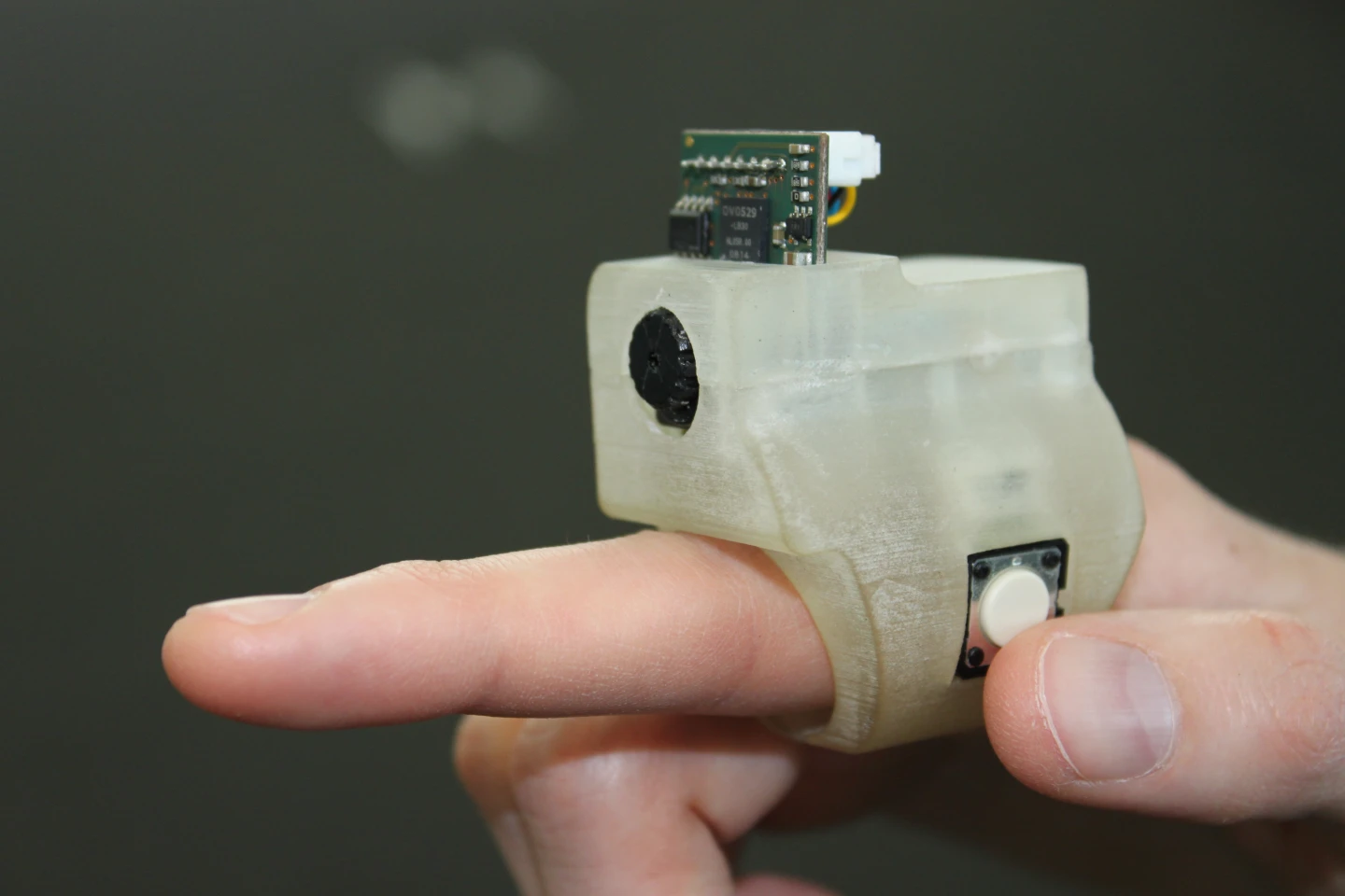 The user points the ring at an object, tells the system what kind of information is needed via a microphone on the earphone cord and then clicks the button on the side of the ring unit to activate the camera and send a photo to a Bluetooth-linked smartphone for processing