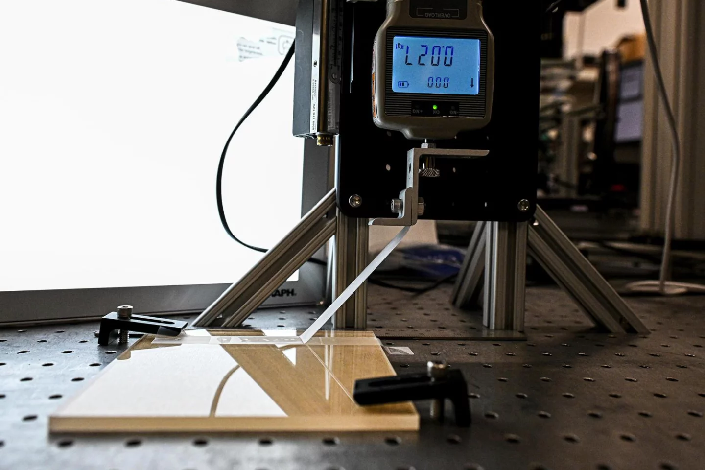 An automated device peels tape to a designated distance, lays it back down, and measures the amount of force needed to peel it again