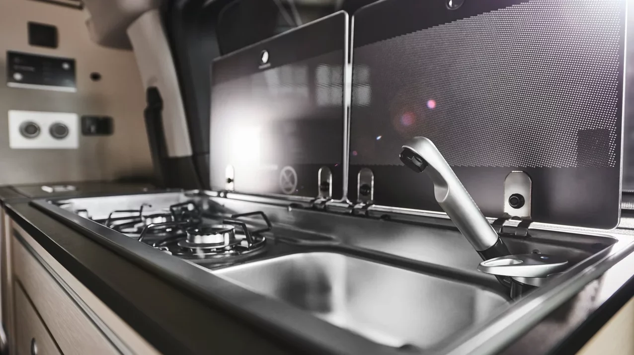 The kitchen has a dual-burner stove and sink below hinged lids