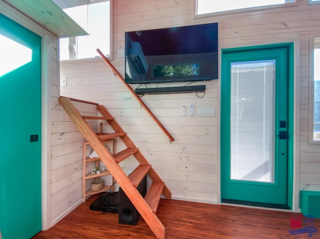 The Sandy tiny house's living room includes a small sofa and some storage, plus a TV