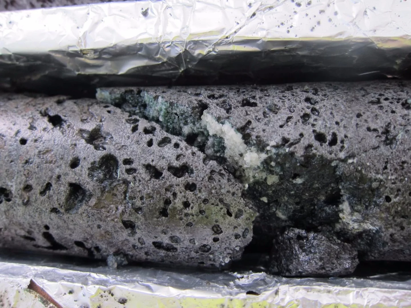 White calcium carbonate crystals can be seen on this basalt rock in Iceland after the addition of CO2 to an underground well
