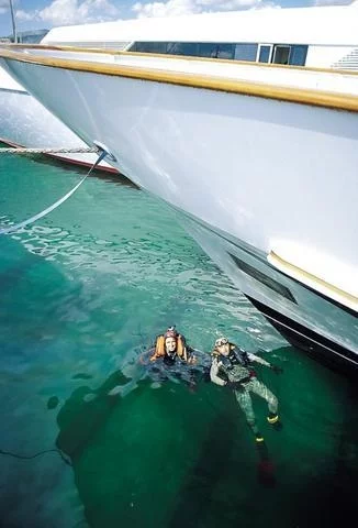 Divers swim beneath the moored yachts, fixing temporary supports before the deck is drained.