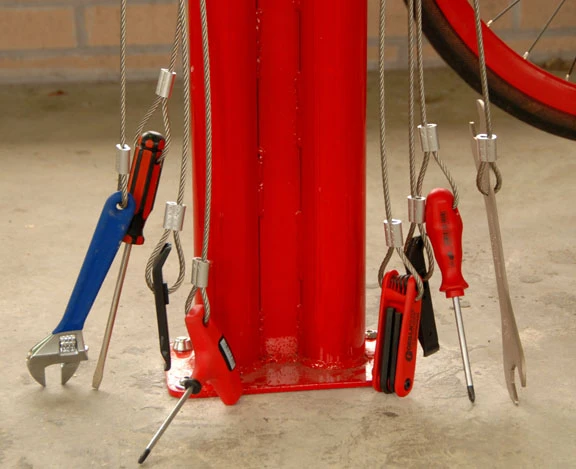 A set of tethered bike tools hangs from the central column of the repair stand