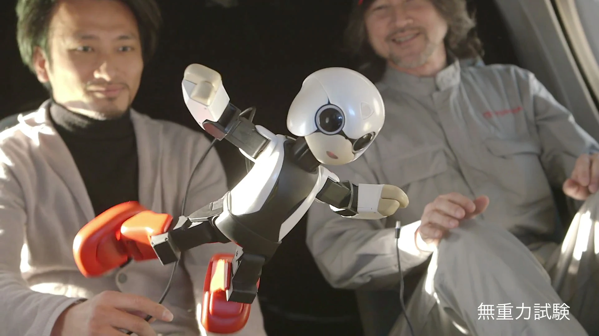 Kibo the Japanese communication robot floats in zero gravity aboard an airplane with its creator, Tomotaka Takahashi (left background)