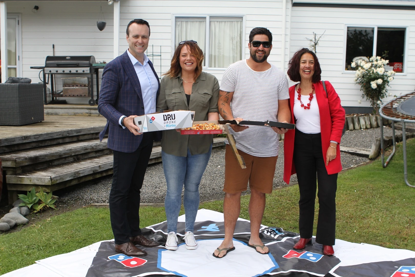 Domino's General Manager Scott Bush (left) and Flirtey's New Zealand Director Samantha Sharif (right) with a couple of happy customers in between
