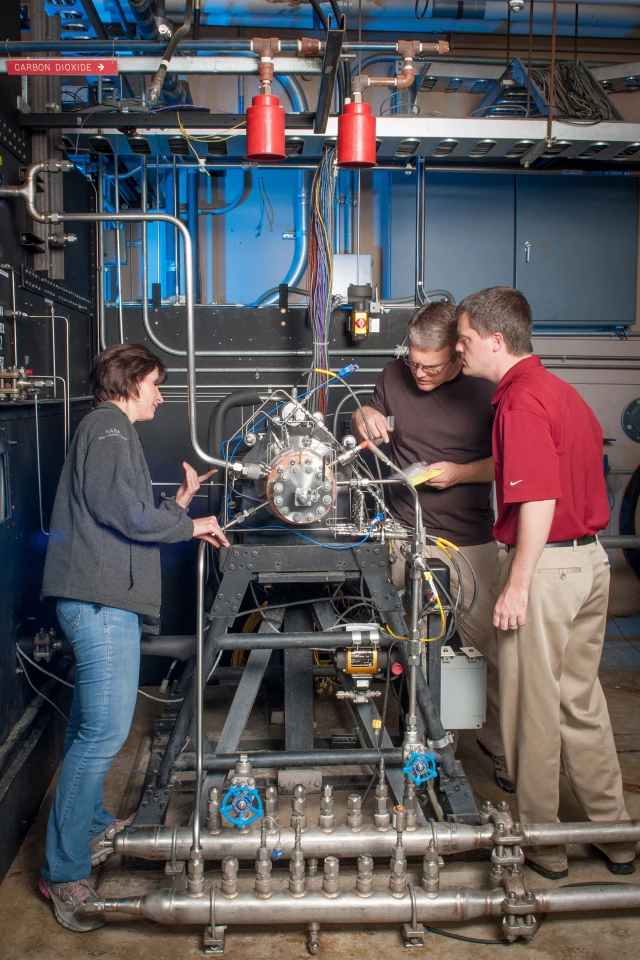 Task lead Tyler Hickman, in red shirt, and technicians inspect the rocket injector assembly