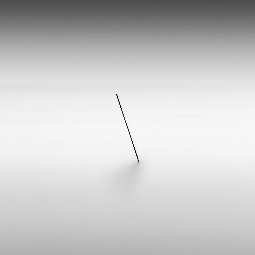 Winner of 3rd place in the Amateur Seascape category: Yaser Sulaiman - Backslash. A minimalist black-and-white long-exposure photo of a slanted rebar (reinforcing bar) sticking out of the water just off the shore of the corniche in Dammam, Saudi Arabia