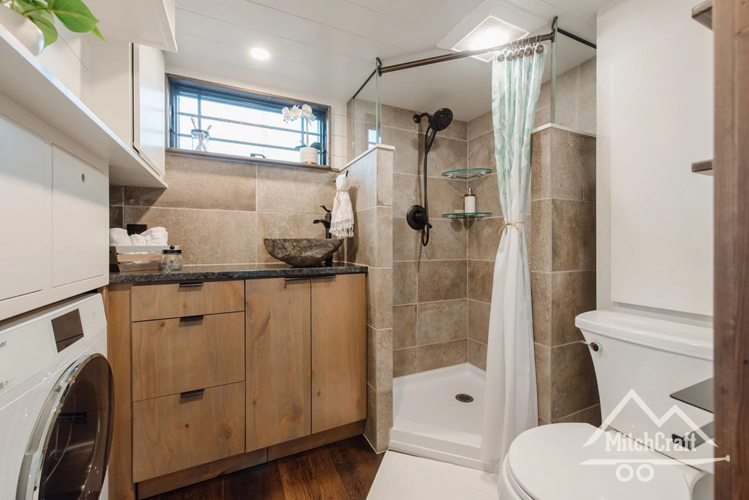 The bathroom features a flushing toilet, sink, and corner shower, as well as some storage space and a washing machine and dryer