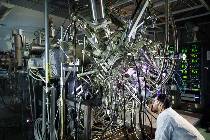 A Sandia materials scientist gazes into a viewport of a molecular beam epitaxy reactor, which will be used to build photonic cooling plates