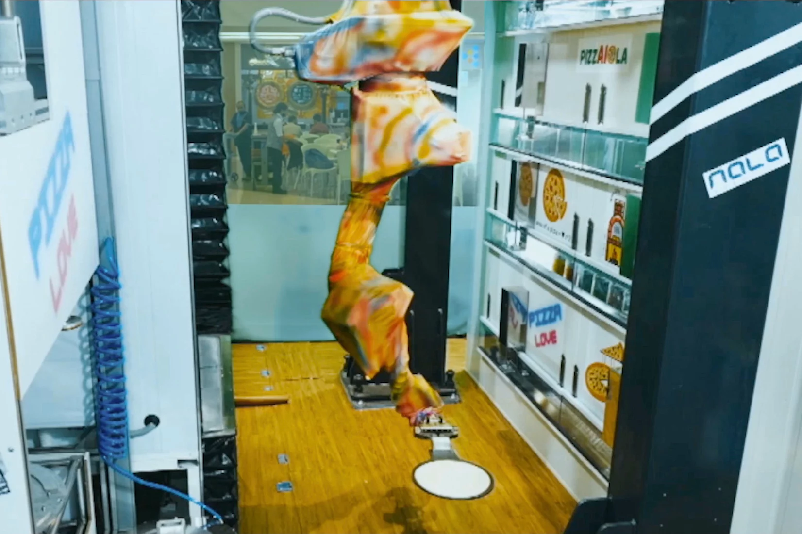 An apparently tie-dye-clad Pizzaiola robot sets about making a pizza