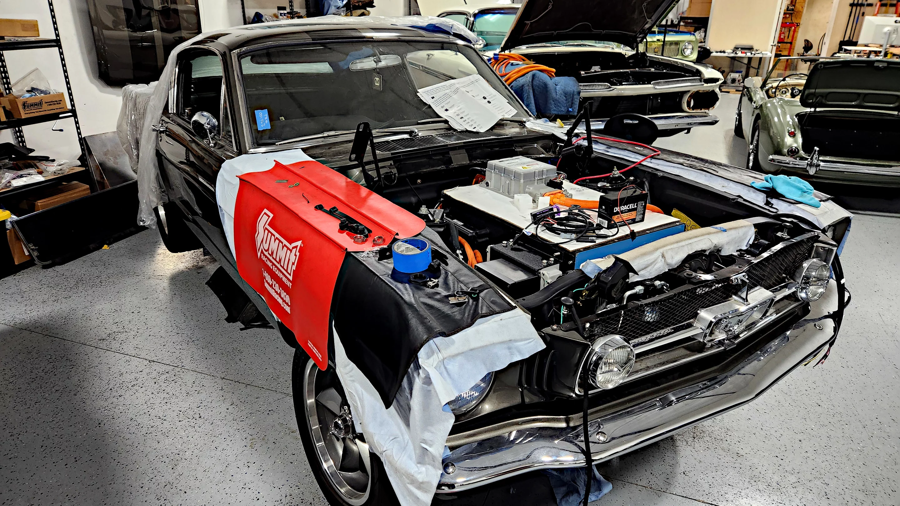 A first-generation Ford Mustang undergoing the EV conversion process at Moment Motors. Behind it, a 1969 Chevrolet Impala is doing the same