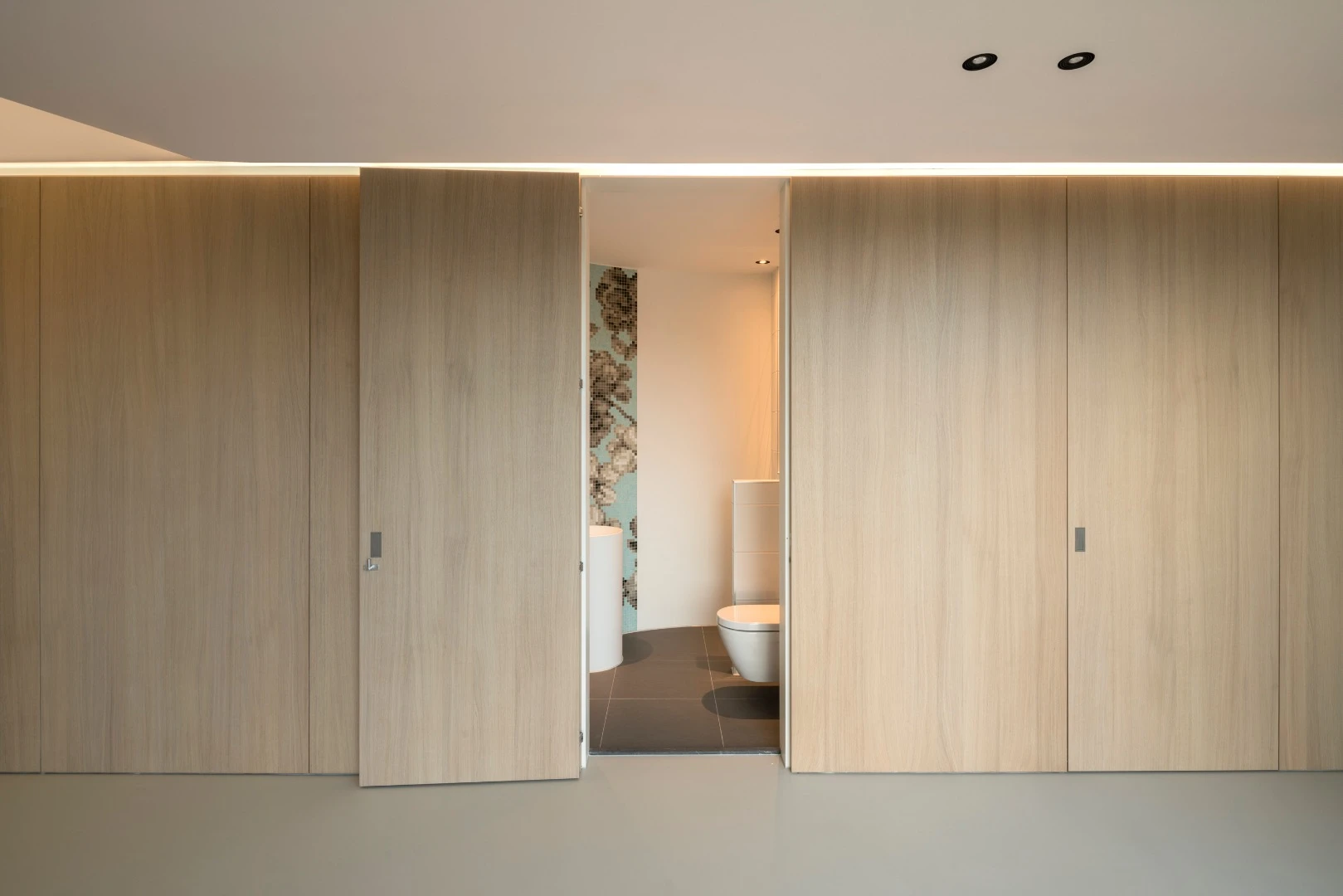 Casa Kwantes' lounge has a long fitted wooden unit that includes kitchen cabinets, pantry, and access to the basement and a guest bathroom