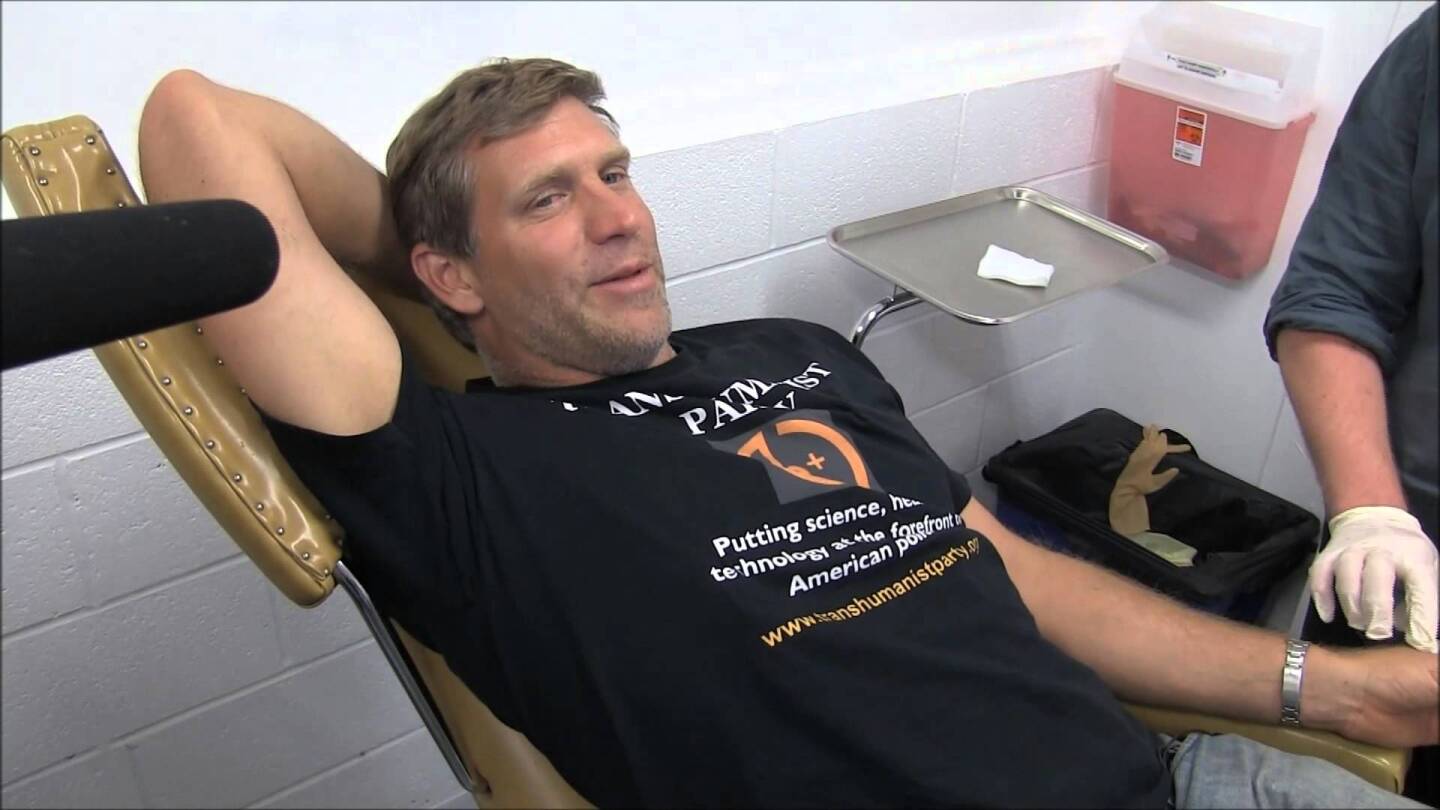 Istvan getting a microchip implanted into his hand during his 2016 tour