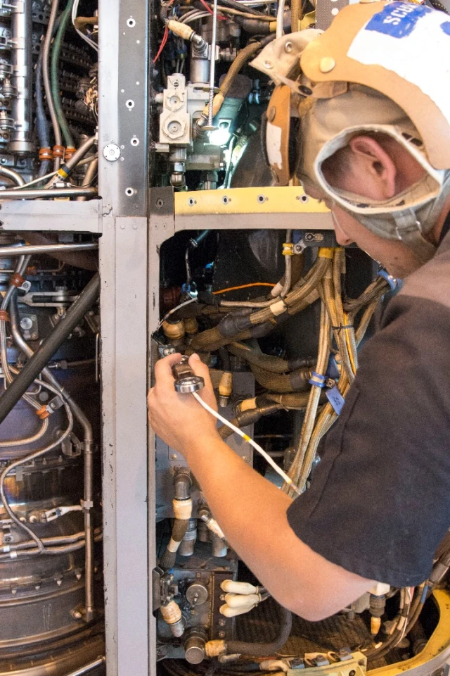 Aviation Mechanic Cody Schwarz works to install a 3-D printed titanium link and fitting on an MV-22B Osprey engine nacelle
