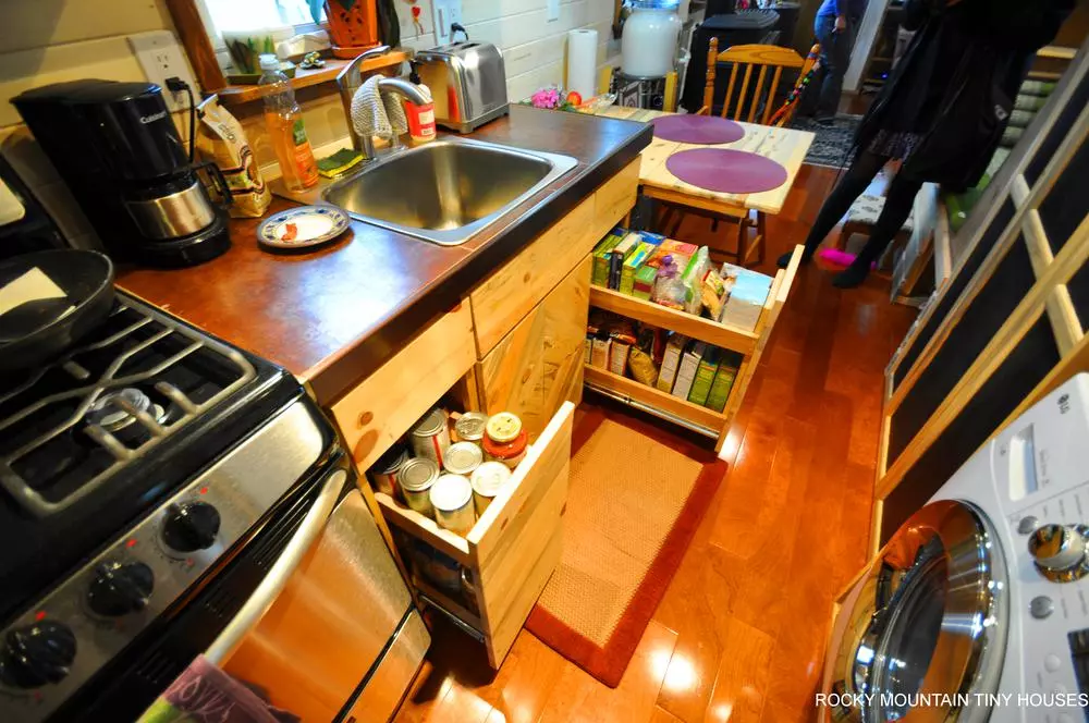 The kitchen in the Red Mountain 34' Tiny House includes two pull-out pantries, a propane-powered range cooker, refrigerator, and sink