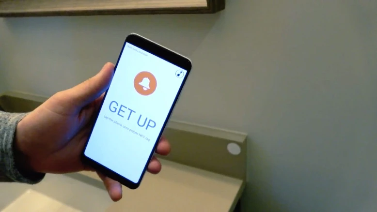 The EzLarm app works with an NFC tag (white disc to the right of the phone)
