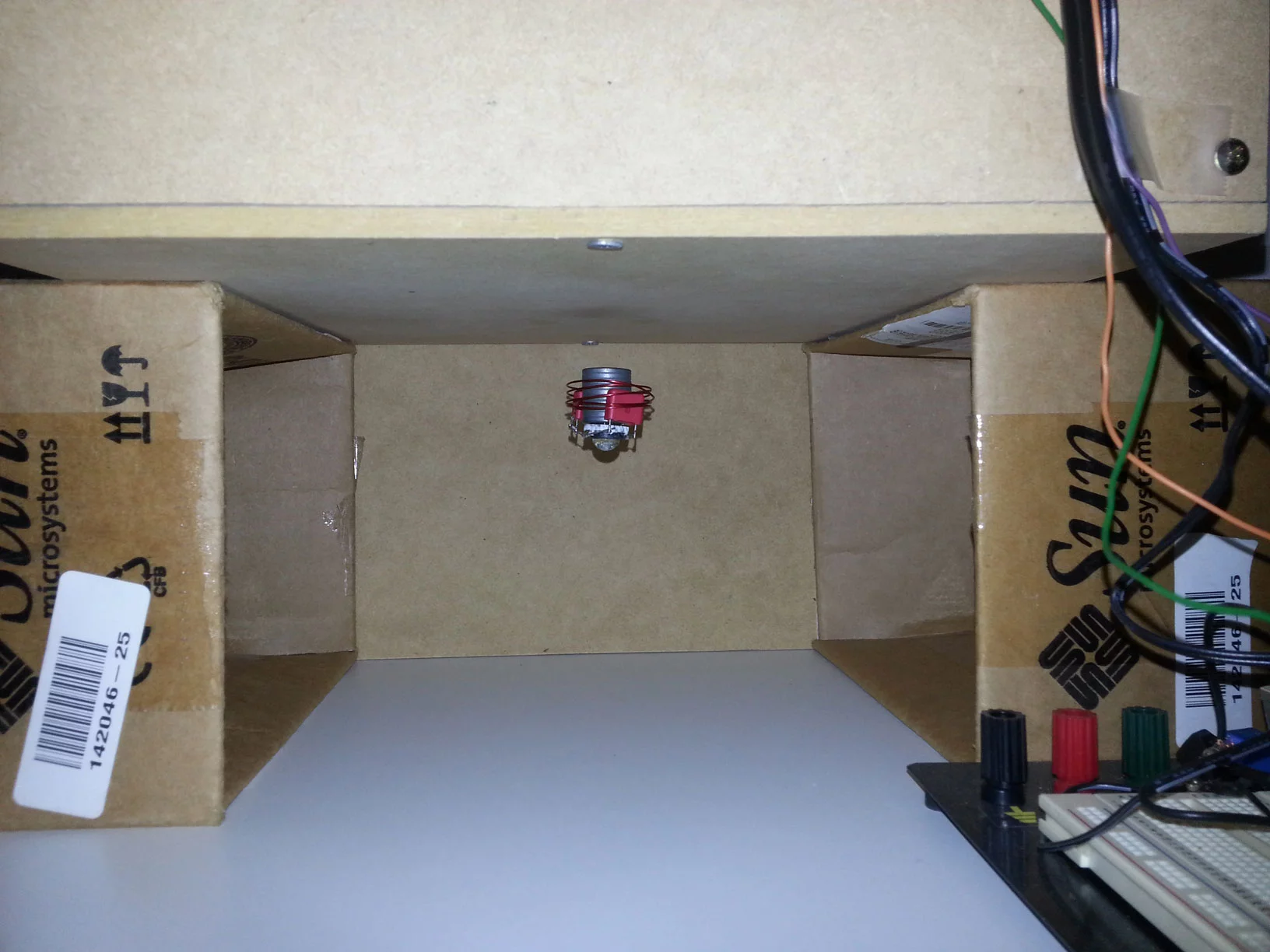The drive coil and wireless mechanism are hidden inside a wooden box raised on two cardboard box columns and, with the power switched on, the LED light floats in the space underneath