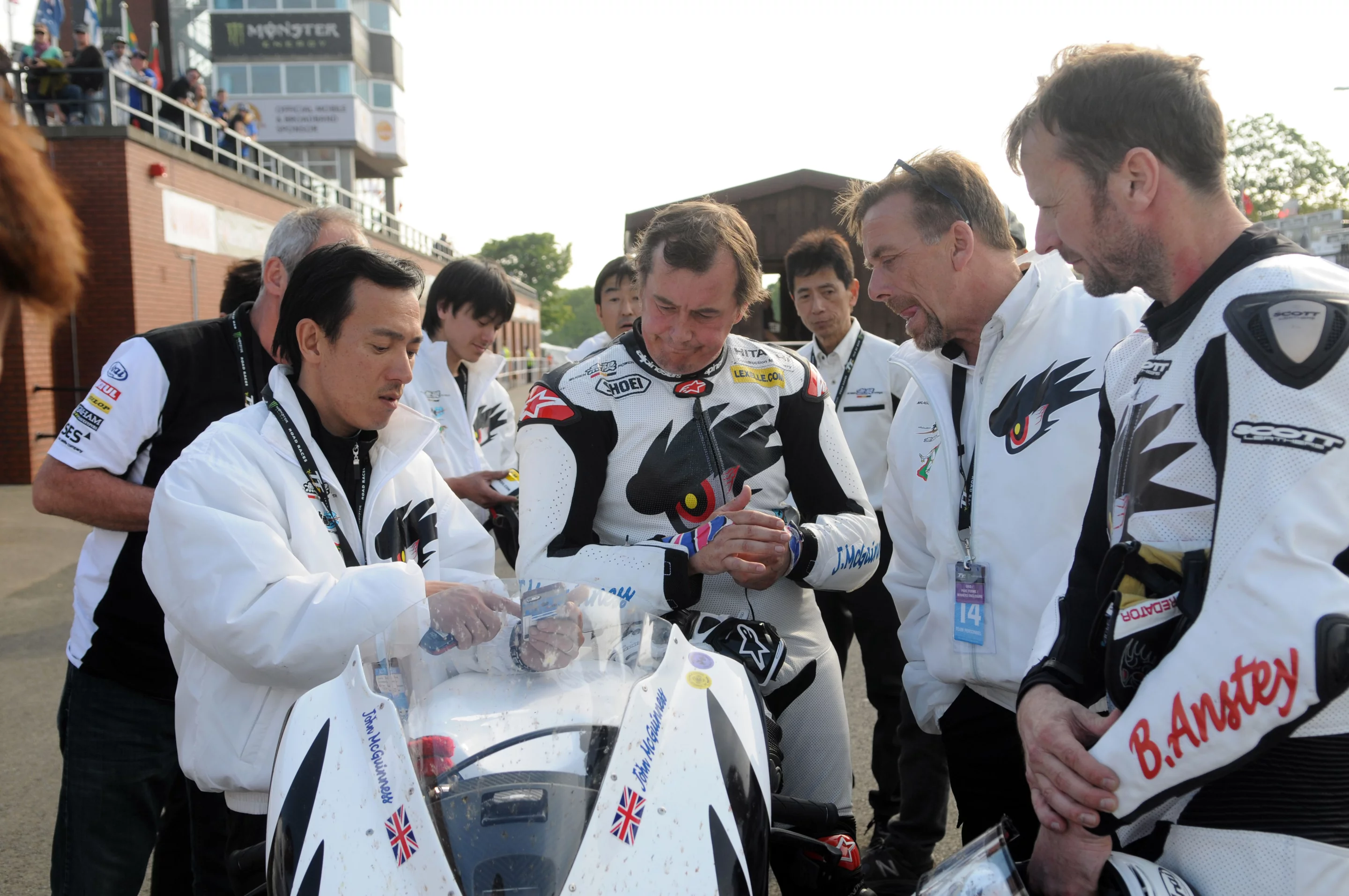 Team Mugen crowd around the times whith John McGuinness (second from left) grimacing at his time and Anstey (far right) observing quietly