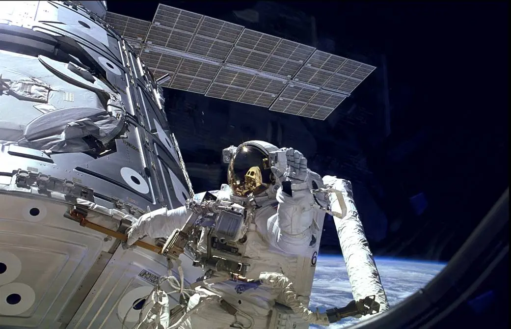 Astronaut James H. Newman waves from outside the International Space Station