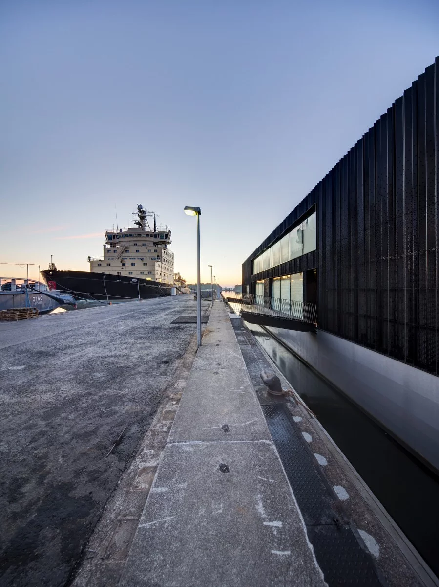 Drawing inspiration from the large black hulls prominent in Arctia's fleet of icebreaker ships, the floating building features a large black steel facade