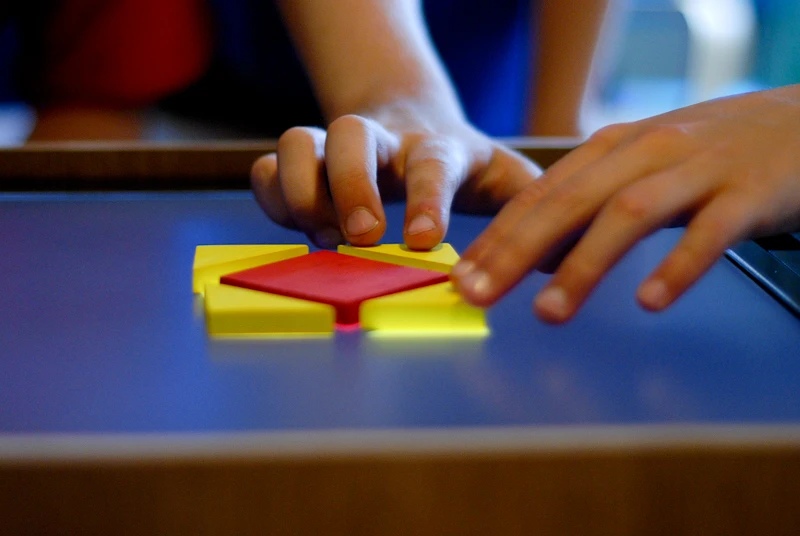 A child arranges corresponding colored blocks over the shapes. With the pieces in place, the "record" button is pressed, and the camera above, which points down at the screen, takes a snapshot