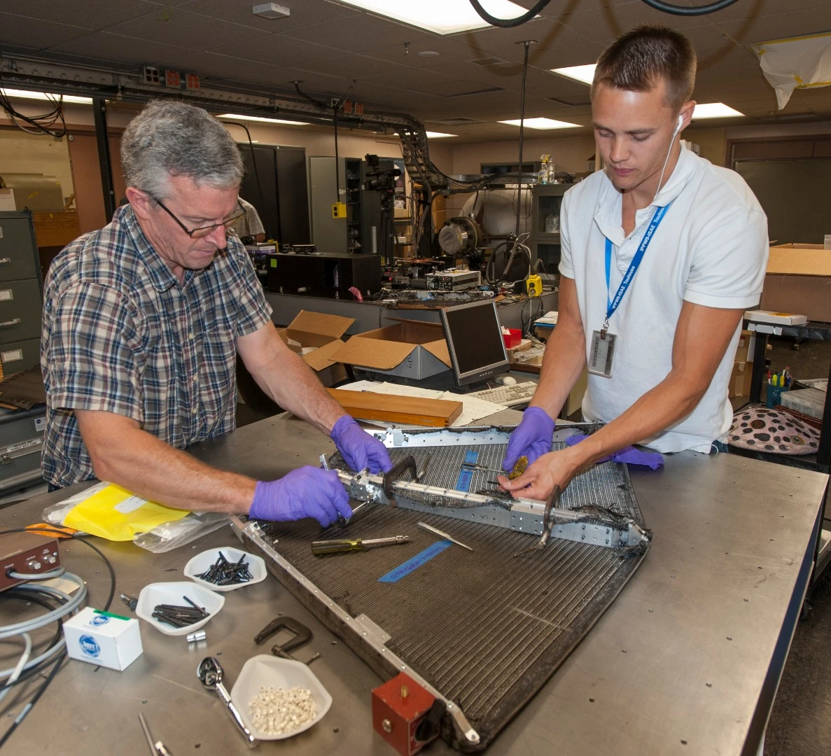 Paul Wercinski, ADEPT project manager and Cole Kazemba, ADEPT system engineer, attach the woven carbon fabric skin to the ribs of an early version of ADEPT in the assembly lab at Ames