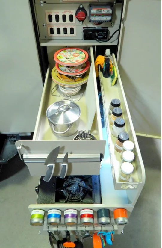 The kitchen includes a main slide-out with stove and sink, along with an upper storage slide-out with magnetic knife holder